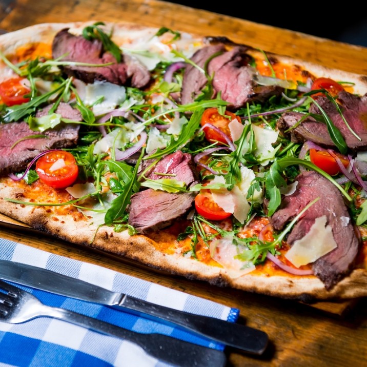 Pizza Bistecca: Tomato, Mozarella, Sliced Flat Iron Steak, Red Onions, Cherry Tomatoes, Olives, Balsamic and Olive Oil Dressing, Rocket and finished with Parmesan Shavings