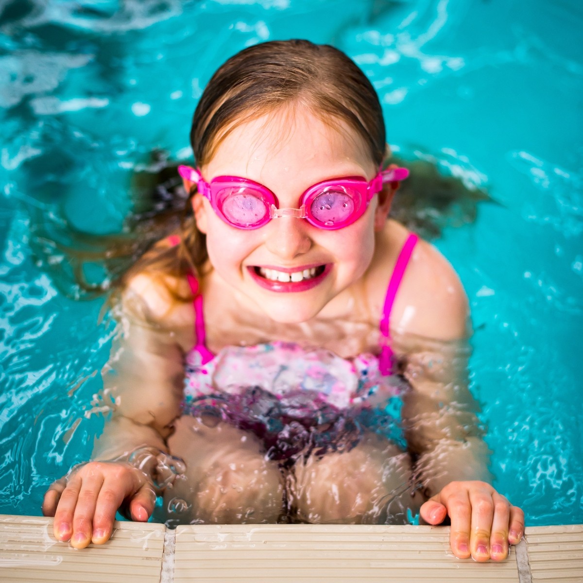 Girl with goggles on at the side of the pool.