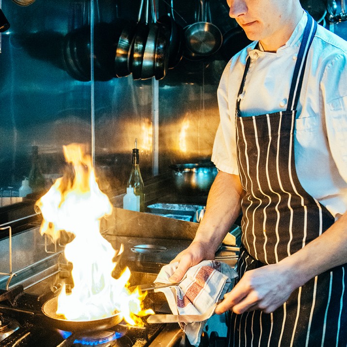 Chef cooking the tasty homemade venison burger over a flaming frying pan at The Venue's new restaurant.