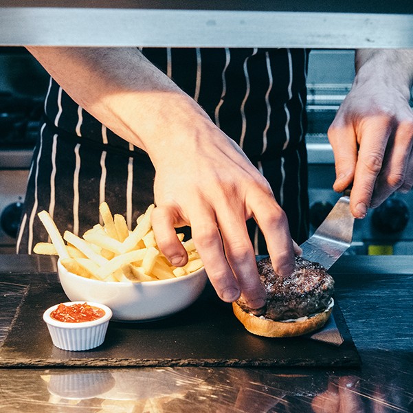 Chef sliding the juicy, plump homemade venison burger onto the brioche bun.