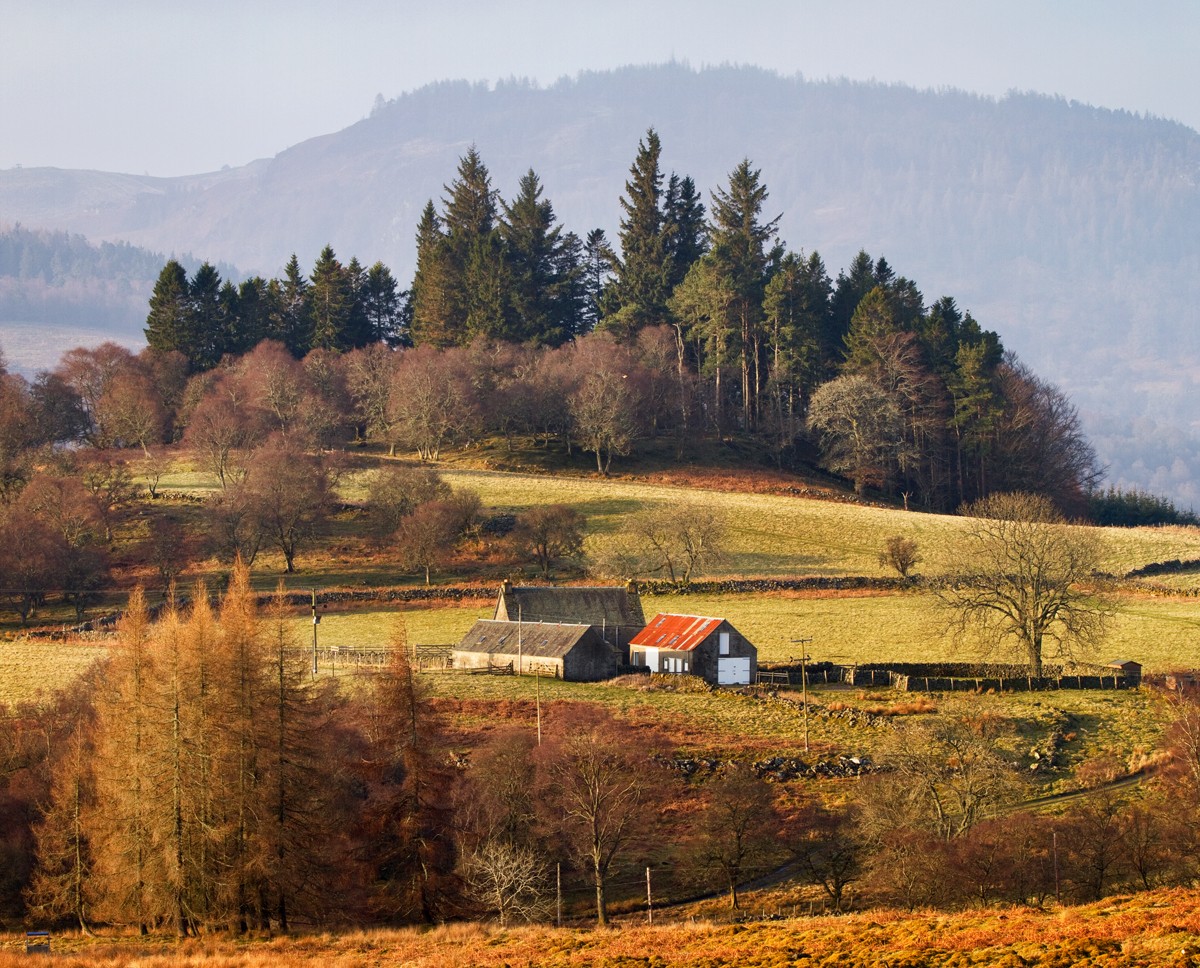 The vast countryside with a field and farmers house nestled into the mountains