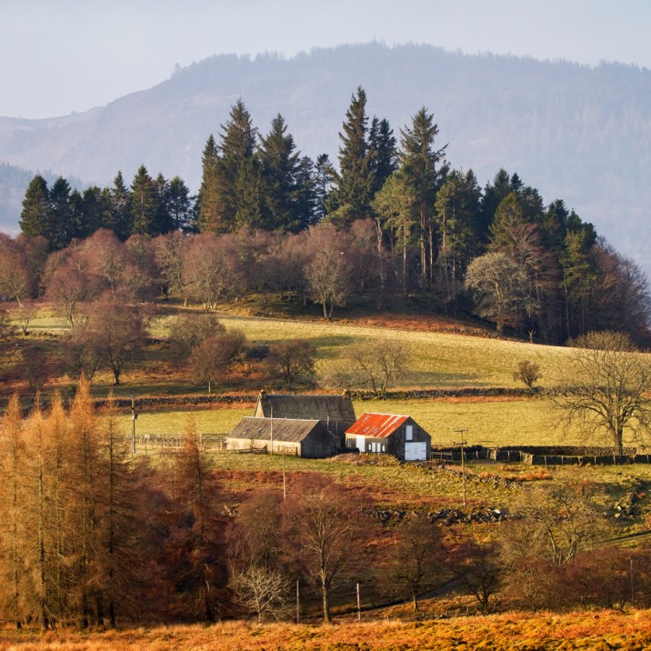 The vast countryside with a field and farmers house nestled into the mountains