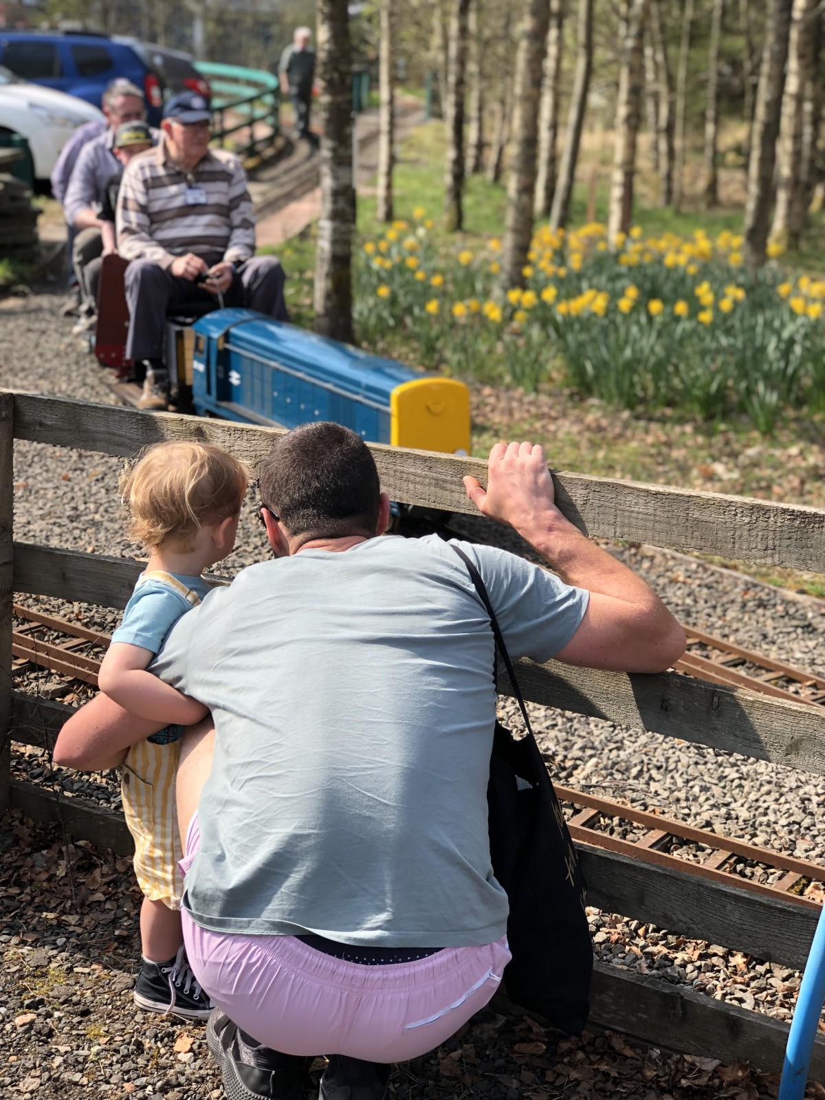A little boy and his daddy peep through the fence to watch the oncoming train at Wester Pickston Railway, Methven, Perthshire